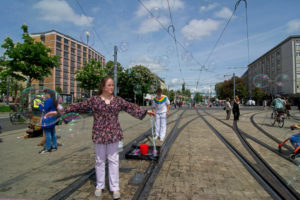 Eine junge Frau steht auf den Gleisen der Straßenbahn und breitet die Hände aus. Um sie herum fliegen viele Seifenblasen.
